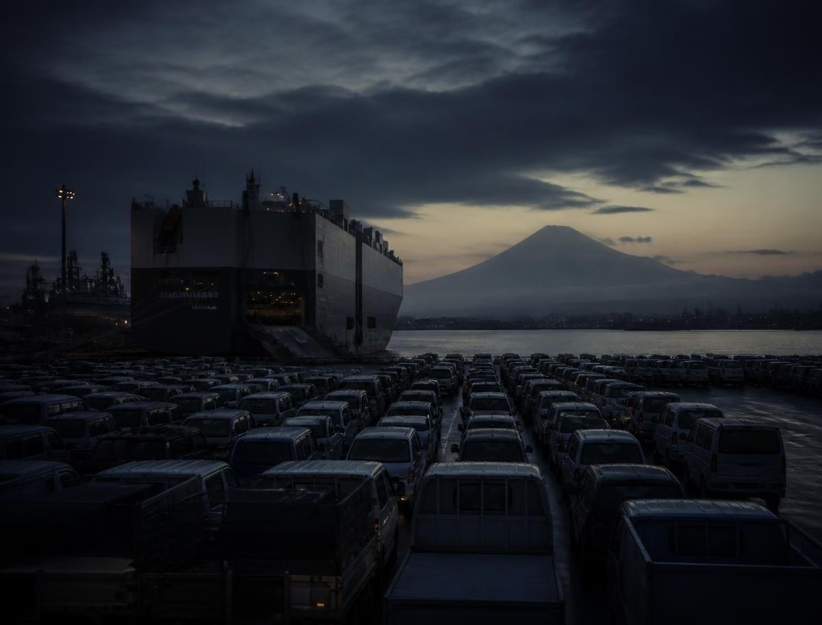 Vehicle carrier ship and rows of used vehicles at a Japanese export port at dusk